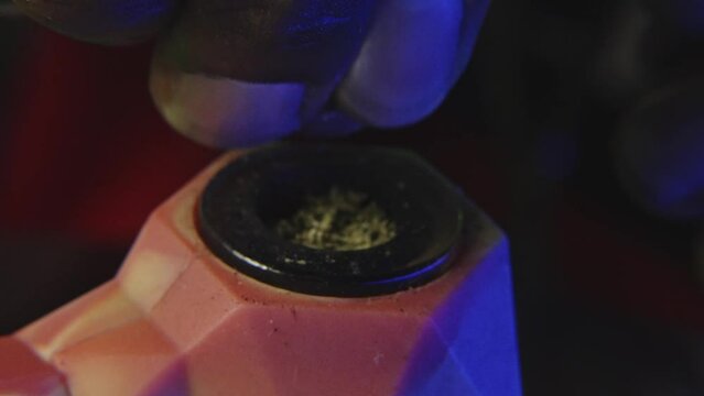 a black mans hand is breaking down marijuana bud to smoke it from a rubber pipe