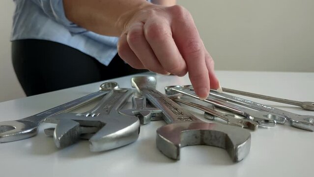 Woman picking up small spanner, multiple wrench tools on table