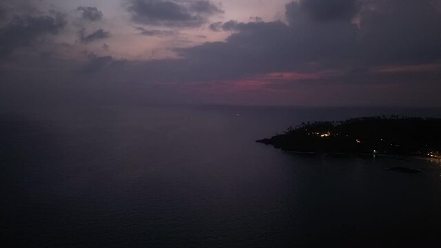 Dramatic sunset skyline over sea, coastal town lights flicker in dusk. Drone captures natures color play, cloud patterns shift rapidly in sky. Evening falls upon exotic locale, view from above.