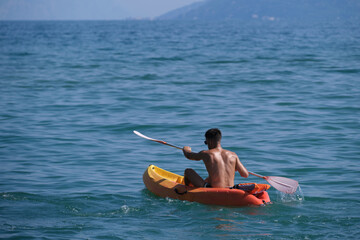 Athletic man on a kayak moving on blue water. A man on an orange kayak in motion on the water, rear view.
