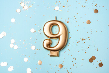 Gold candle in the form of number nine on blue background with confetti.