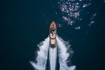 Classic Italian wooden boat fast moving aerial view. Top view of a wooden powerful motor boat. Luxurious wooden boat fast movement on dark water.