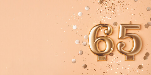 65 years celebration. Greeting banner. Gold candles in the form of number sixty five on peach background with confetti.