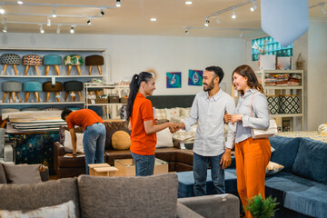 male and female customers shake hands with a female store employee while buying products in furniture department store