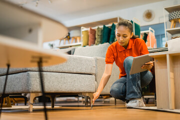 female shop clerk uses a tablet checking the condition of sofa legs in a furniture store