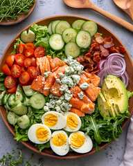 Salmon cobb salad in wood plate, there is buttery spring salmon, romaine lettuce, endive, watercress greens, boiled eggs, bacon, crumbled blue cheese, avocado, tomatoes and slices of red onion