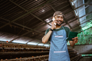 Businessman reading passbook and making phone calls at chicken farm