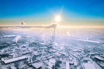 Bright sun shines over the smoking chimneys of a metallurgical plant. Winter view from above