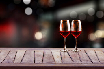 Red wine glass on wooden plank with wine bottle rack as background and blurry wine drinking counter background..