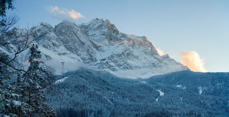 Obraz premium A bottom up view to the ice cold and with snow covered Zugspitze mountain chain and the surrounding forest nature landscape