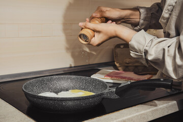 Unrecognizable woman adding salt to eggs in skillet