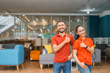 smiling man and woman with thumbs up standing in front of couch in furniture store department