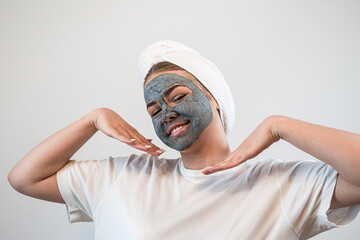 young caucasian woman in towel on head with black clay or mud facial mask isolated on white