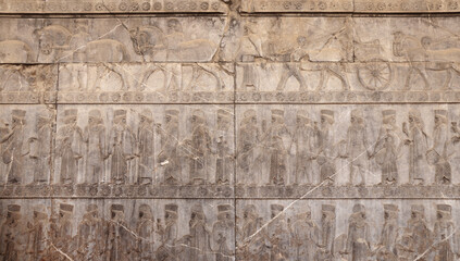 Ancient wall with bas-relief with assyrian warriors with spears,  horses, chariots, Persepolis, Iran