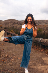 Young woman wearing overalls kicking air on a hiking trail
