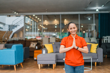 Young woman with welcome hand gesture standing in front of many couch in furniture store