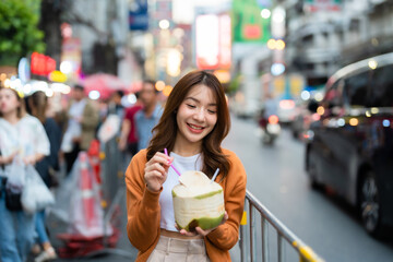 Young asian woman traveller standing and drinking coconut water. Beauty traveller female in city lifestyle chinatown street food market Bangkok, Thailand - obrazy, fototapety, plakaty