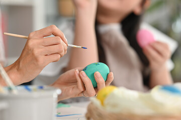 Closeup mother and her daughter painting easter eggs in living room, getting ready for holiday