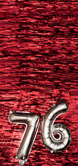 Silver foil balloon number 76 on a background of red tinsel decoration. Birthday greeting card,...