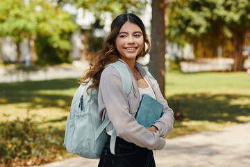 Portrait of smiling high school student with backpack and planner standing on school campus - obrazy, fototapety, plakaty
