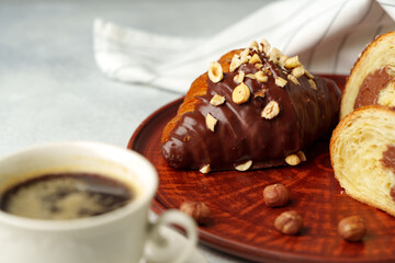 Chocolate croissant on clay plate with cup of coffee on table