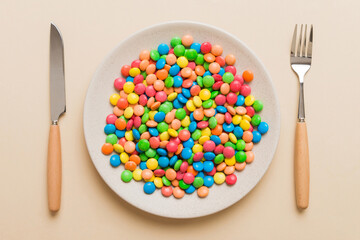 cutlery on table and sweet plate of candy. Health and obesity concept, top view on colored background