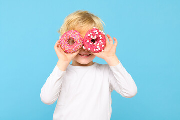 Cute little boy with blond hair and freckles having fun with glazed donuts. Children and sugary...