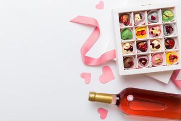 Bottle of red wine on colored background for Valentine Day with gift and chocolate. Heart shaped with gift box of chocolates top view with copy space