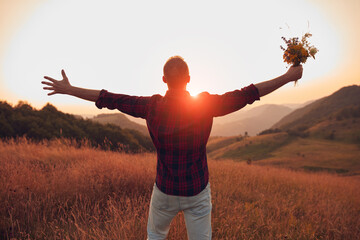 Man with arms wide open holding field flowers in nature.