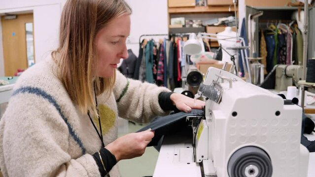 Seamstress using a serger overlock machine in slow fashion textile studio.