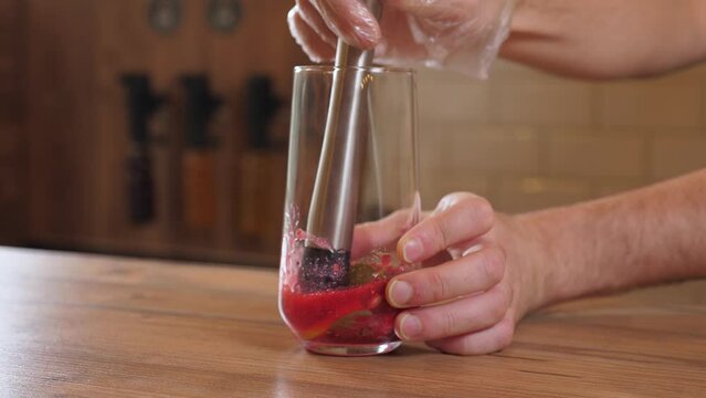 Close-up of the bartender squeezing the juice from a lemon in a glass with a special mudler, the process of making lemonade with lemon and berry juice in the bar.