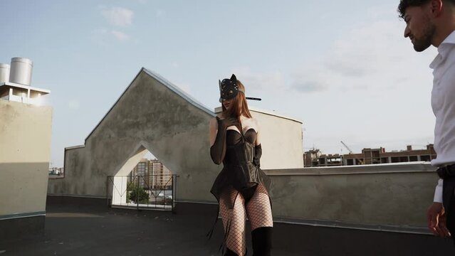 A woman photographer takes a photo of a couple in love wearing a cat mask on the roof against a sunset background. BDSM photo shoot concept