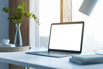 Modern designer desktop with white mock up laptop, various objects and window with city view in the background. 3D Rendering.