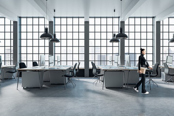 Pretty blurry woman walking in modern coworking office interior with large panoramic windows with city view, lamps, concrete flooring and other objects.
