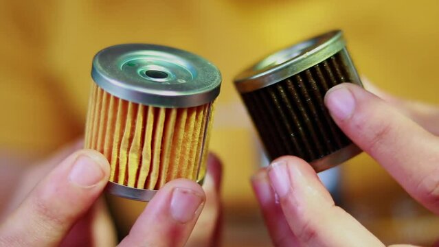 Hand-holding uses an engine oil filter and a new engine oil filter, A use and a new oil or fuel filter of the motorcycle is in the hands of a motorcycle mechanic,