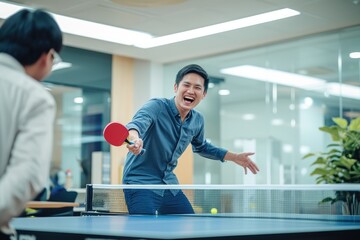 Happy young asian man having fun playing table tennis with colleague in an office zone. 