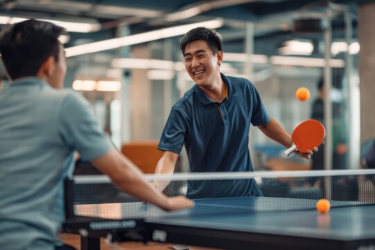 Happy young asian man having fun playing table tennis with colleague in an office zone. 