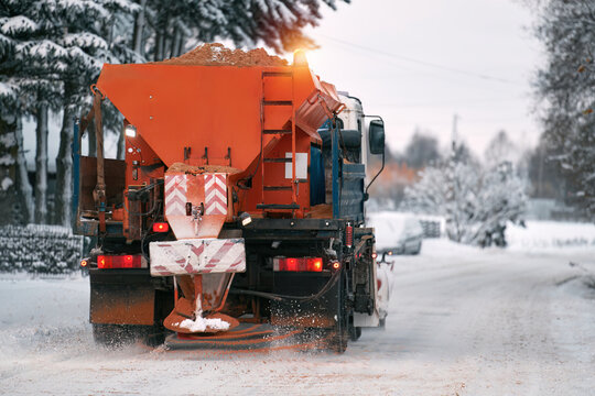 Road maintenance in winter. a tractor equipped with a spreader sprays a salt and sand mixture on the icy and snowy road. The vehicle belongs to the municipal service that melts the snow