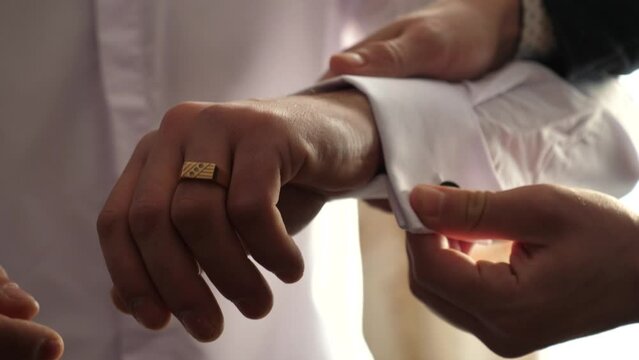 A man is helped to put on the cufflink of a white shirt. Slow motion