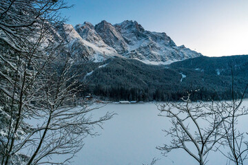 Spotting through the forest to the frozen Eibsee lake with the Zugspitze landscape at the background