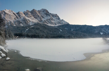 Spotting through the forest to the frozen Eibsee lake with the Zugspitze landscape at the background