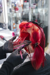 close-up hairdresser colorist dyes client's hair red in a beauty salon, vertical photo
