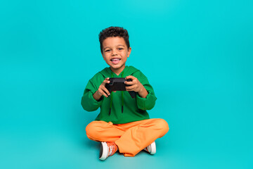 Photo of adorable carefree boy dressed stylish green clothes playing playstation isolated on cyan...