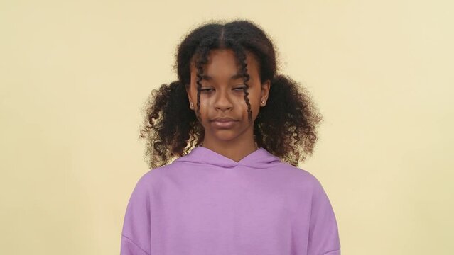 Slow motion, portrait of a dark skinned girl, teen girl looks into the camera, close-up view of eyes, serious look, facial features, beige background.