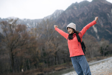 Peak reflection, Asian woman in a pink fleece, standing alone by the water. Elegant portrait showcasing success, happiness, and the scenic horizon of a journey.