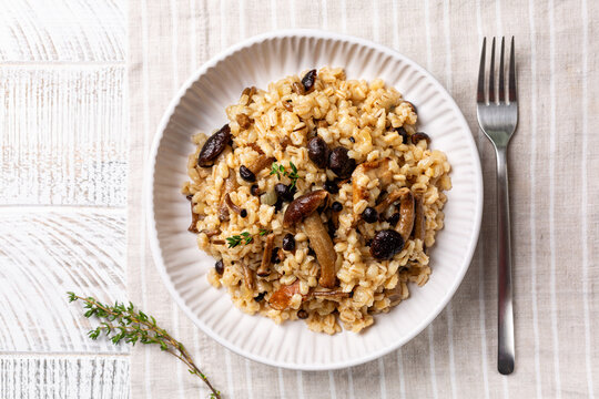 Top view of mushroom barley risotto or orzotto in a white plate on a line  tablecloth. Made with pioppini and porcini mushrooms. Italian Vegan food.