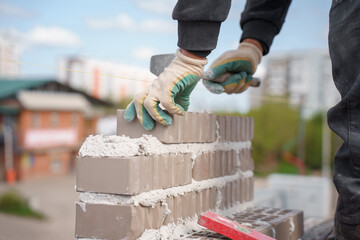 Close-up of mason's hands laying brickwork on construction site - obrazy, fototapety, plakaty