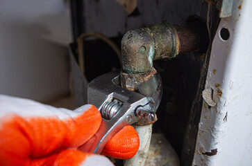 An adjustable wrench in the hands of a service engineer to disconnect a gas pipe in an old gas kitchen stove.