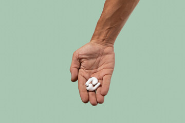 Male hand holding white earbuds on green background.