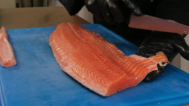 Cutting raw salmon fillet. The cook cuts off the unusable parts of the fish.